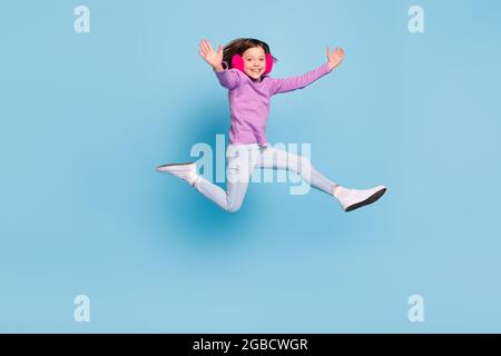 Full length body size photo small girl jumping wearing fluffy headphones isolated pastel blue color background Stock Photo