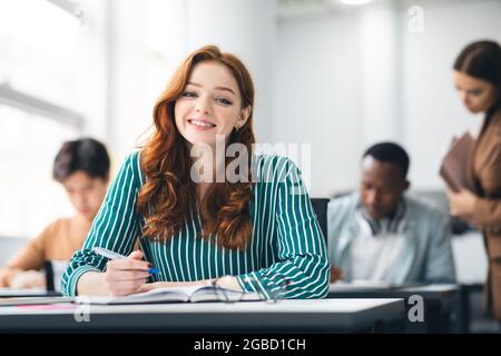 Smiling female student sitting at desk writing in notebook Stock Photo