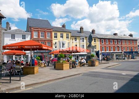 Visitors people sitting under Welcome Brecon umbrellas at picnic tables outside St Marys church in town centre summer 2021 Powys Wales UK KATHY DEWITT Stock Photo