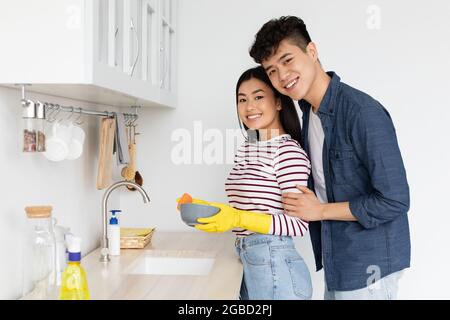 Pretty asian lady washing dishes, wearing gloves Stock Photo