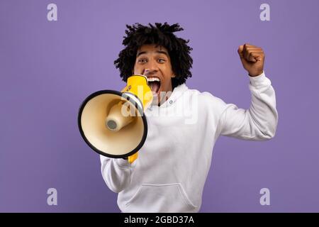 Agitated black teenager shouting into megaphone over violet studio background Stock Photo