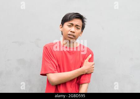 Closeup of a young man in a red T-shirt on the background of a gray wall. Stock Photo