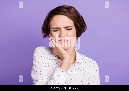 Portrait of young girl closed eyes arm on cheek suffer from teeth pain bad mood isolated on purple color background Stock Photo