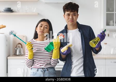 Bored asian man and woman holding cleaning tools Stock Photo