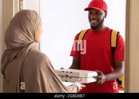 Black deliveryman holding and giving pizza boxes to muslim customer Stock Photo