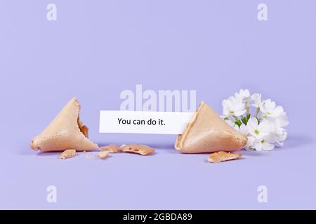 Motivational text in fortune cookie saying 'You can do it' on purple background with flower Stock Photo