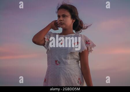 Young Indian woman with a beautiful white dress enjoying the wind during sunset Stock Photo