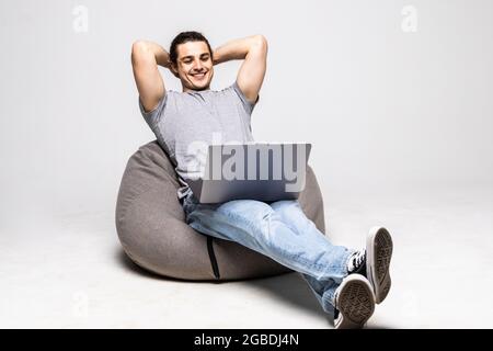 Young man with laptop sitting on beanbag chair against white background Stock Photo