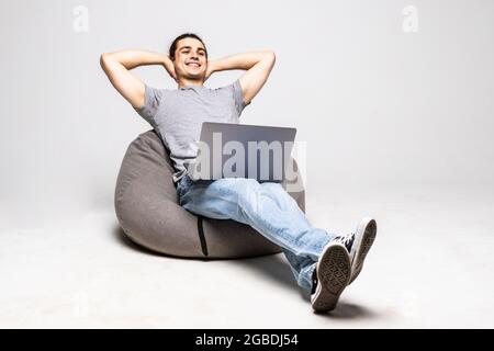 Young man with laptop sitting on beanbag chair against white background Stock Photo
