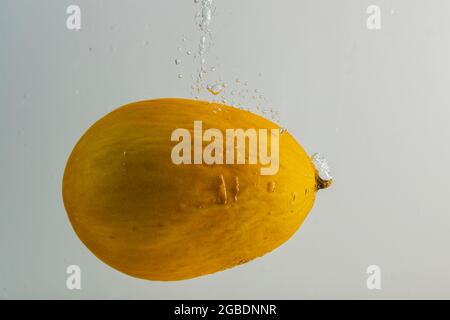 Close up view of yellow melon falling in water on grey background.  Gorgeous backgrounds. Stock Photo
