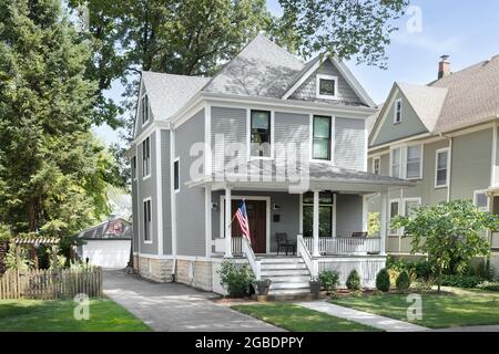 A beautifully renovated Victorian home with a grey and white siding, a covered front porch and a driveway leading to the backyard. Stock Photo