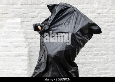 Photographer photographing in the rain while wearing a plastic black waterproof barbage bag as a poncho to protect herself from the bad wet cold weath Stock Photo