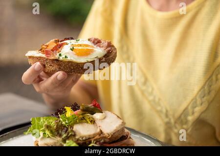 Woman eating a healthy homemade club sandwich dish with fresh ingredients such as tomato, salad, lettuce, bacon, cauliflower and chicken and a sunny s Stock Photo
