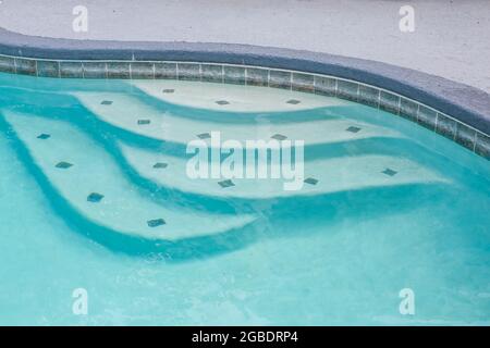 Pool steps in a large free form gray grey accent swimming pool with turquoise blue water Stock Photo