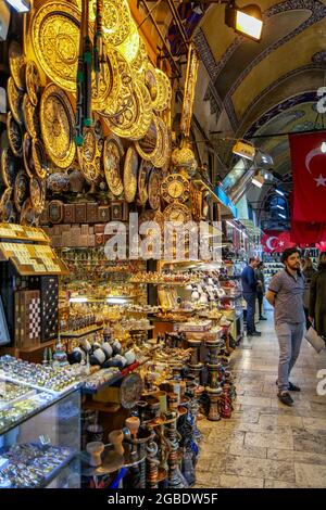 View of several peoplewalking and standing in an arched passageway, including a bearded man, in full length, facing the camera, with a serious expression, walking next to a shop displaying colorful souvenirs, including plates, chess sets, inlaid boxes, tabla drums, and nargiles, water pipes, or hookahs, with stone-paved floors visible at right, and Turkish flags visible in the background, located in the Grand Bazaar, a large indoor shopping district, constructed by the Ottomans between the 15th and 18th centuries, in the Fatih district of Istanbul, Turkey, November 11, 2017. (Photo by Smith Co Stock Photo