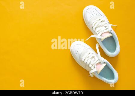 White sneakers isolated on yellow background with copy space. Top view. Flat lay. Sportswear. Pair of woman shoes. Stock Photo