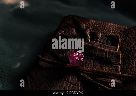 Close-up image of a pink transparent 20-sided RPG die on a pink a brown leather notebook Stock Photo