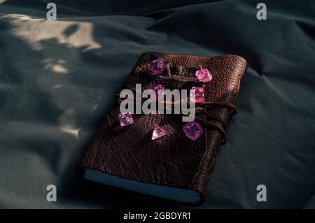 Image of pink transparent gaming dice on a leather bound notebook  partially lit by the sun Stock Photo