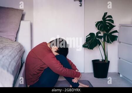 Depressed and sad woman huging her knee and sitting on the floor in the bedroom. Troubled with domestic violence, unwilling pregnancy, abortion Stock Photo