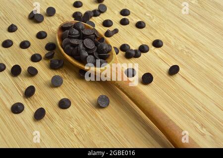 Delicious dark chocolate drops in wooden spoon, on cutting board Stock Photo