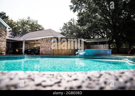 A large free form gray grey accent swimming pool with turquoise blue water in a fenced in backyard in a suburb neighborhood. Stock Photo