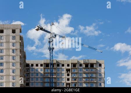building process of large residential apartment building with crane on cloudy sky background. Stock Photo