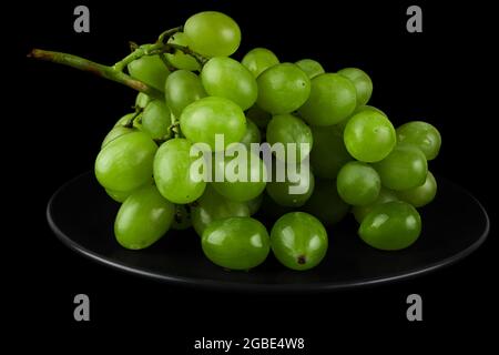 A bunch of table grapes, white pouring, on a black plate, on a black background Stock Photo