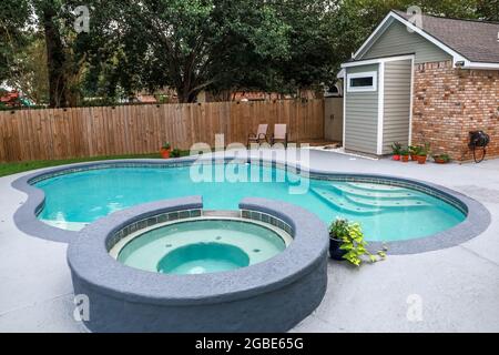 A large free form gray grey accent swimming pool with turquoise blue water in a fenced in backyard in a suburb neighborhood. Stock Photo