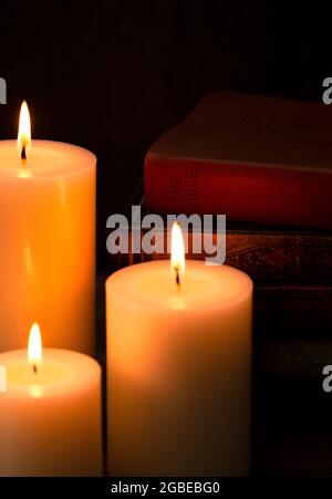 Three Pillar Candles Lit in a Dark Room with a Bible Stock Photo
