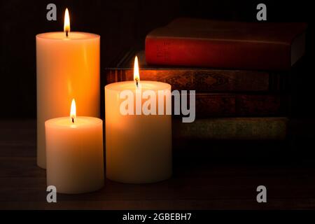 Three Pillar Candles Lit in a Dark Room with a Bible Stock Photo