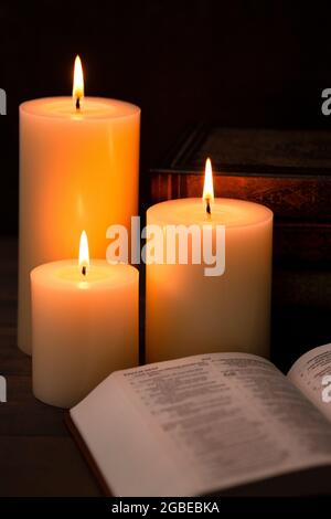 Three Pillar Candles Lit in a Dark Room with a Bible Stock Photo