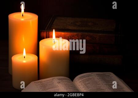 Three Pillar Candles Lit in a Dark Room with a Bible Stock Photo