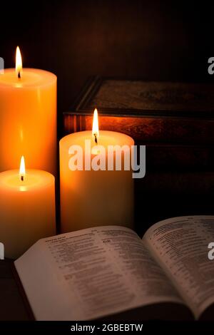 Three Pillar Candles Lit in a Dark Room with a Bible Stock Photo