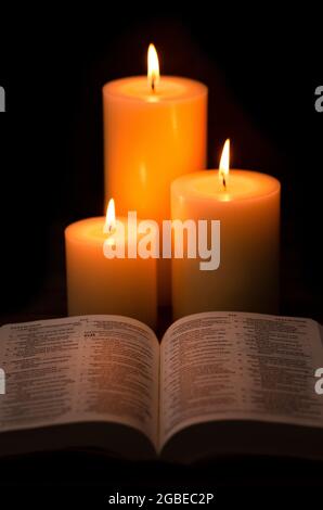 Three Pillar Candles Lit in a Dark Room with a Bible Stock Photo