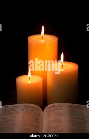 Three Pillar Candles Lit in a Dark Room with a Bible Stock Photo
