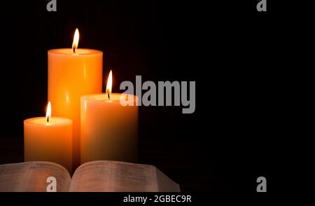 Three Pillar Candles Lit in a Dark Room with a Bible Stock Photo