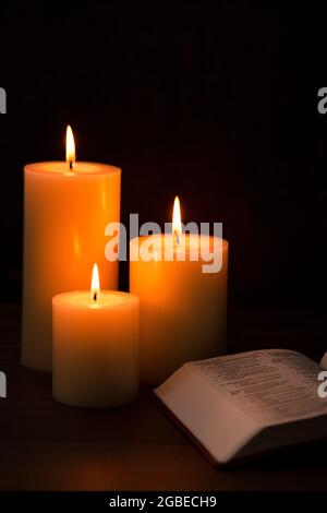 Three Pillar Candles Lit in a Dark Room with a Bible Stock Photo