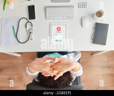 Top view of a female doctor stretching sitting at the desk in her medical office Stock Photo