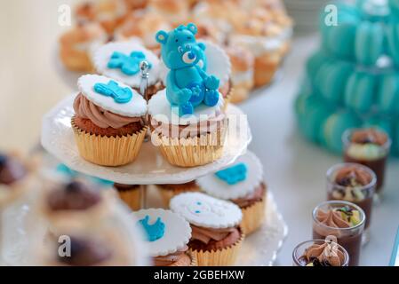 Adorable cupcakes with blue royal icing bear figurines and chocolate cream, sweet treats set on tiered white plates and prepared for a dessert bar Stock Photo