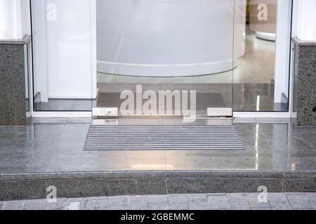 granite gray porch step with a foot mat at the entrance to the central door made of tempered glass on floor iron hinges modern architecture office sty Stock Photo