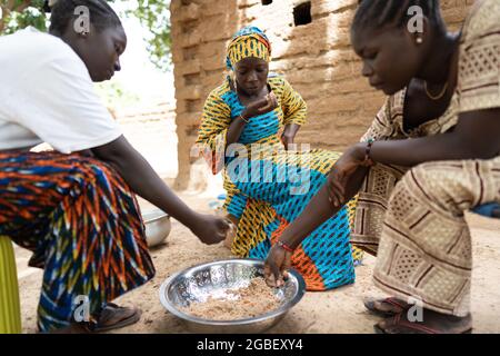 In this image, black women are sharing their meal according to West African rural tradition, sitting separeted from the men and children of their fami Stock Photo