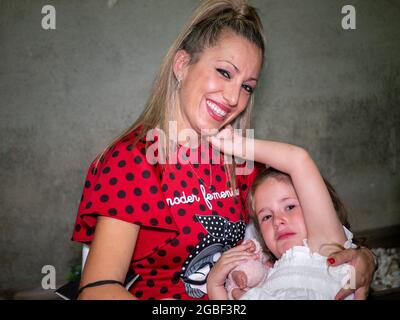 Smiling Spanish woman is holding her child who is upset with something Stock Photo