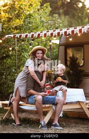 Vacation in motor home: young family relax outdoors near trailer camping in forest on trip in rv van Stock Photo