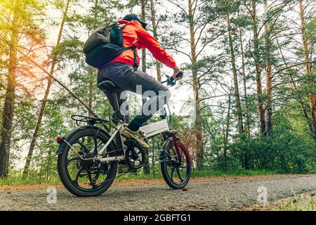 A cyclist rides on a bike path in the forest. Riding an electric modern bicycle. Cool fashionable bike with alloy wheels. A cyclist rides against the Stock Photo