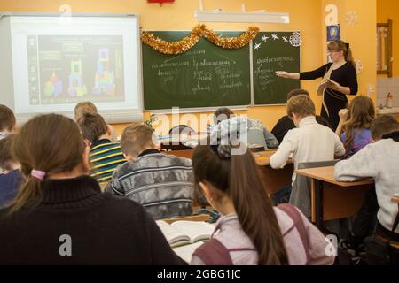 Tula, Russia - January 18, 2013: Beautiful young teacher woman standing near green classic blackboard with chalk in a middle school class during a les Stock Photo