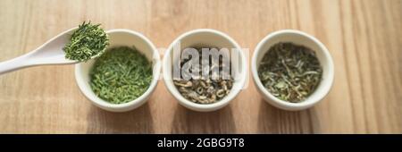 Green tea chinese loose leaf types selection in teacups panoramic banner background on rustic wooden tray. Focus on spoon header. Matcha, royal white