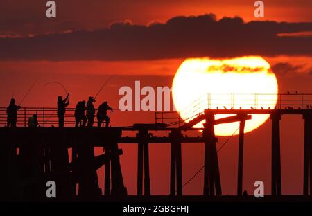 Anglers, hoping to catch mackerel and other fish, cast from the end of Blyth pier in Northumberland as the sun rises over the north east coast of England. Picture date: Wednesday August 4, 2021. Stock Photo