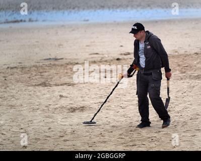 Man with metal detector looking for valuable lost objects on holiday beach. Stock Photo
