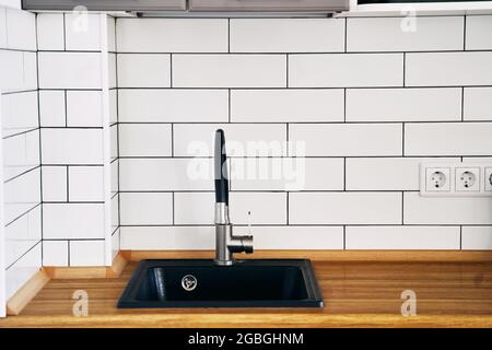 Stylish black sink and faucet on a wooden countertop in a kitchen set close-up Stock Photo