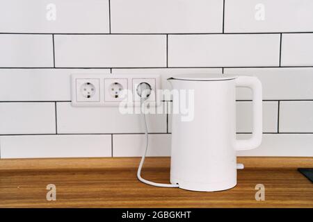 White electric kettle stands on a gray table plugged into a power outlet  Stock Photo - Alamy